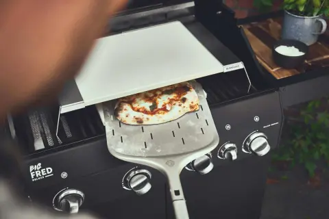 Frisch gebackene Pizza auf dem Pizzaschieber, bereit für den Gasgrill.