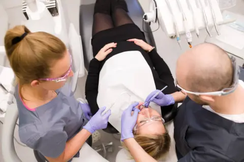 Dentyści wykonują fluoryzację zębów u pacjentki.