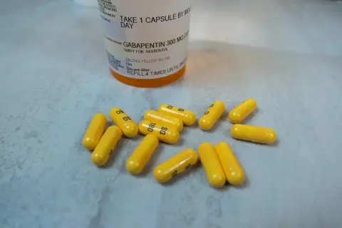 Żółte kapsułki leku Gabapentin 300 mg rozsypane obok butelki z lekiem.