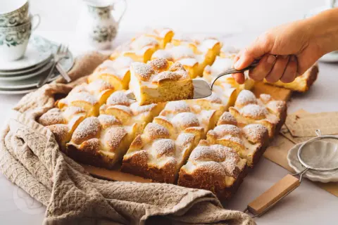 Ein frisch gebackener Ploatz, mit Puderzucker bestäubt, wird aus der Form gehoben. Ein köstliches Rezept für süße Momente.
