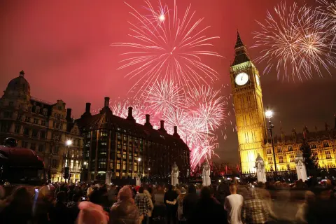 Fuegos artificiales iluminan el cielo sobre el Big Ben y el Parlamento, celebrando las festividades inglesas con una multitud expectante.