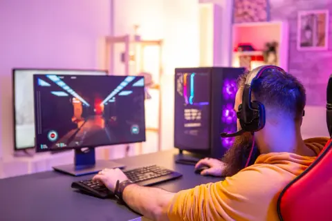 Gamer mit Headset spielt am PC. Die leuchtende Grafik auf dem Monitor und der beleuchtete PC-Tower deuten auf die Vorteile eines Twitch Partners hin.