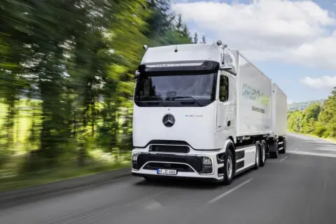 Un camion électrique Mercedes eActros GigaSpace roule sur une route bordée d'arbres.
