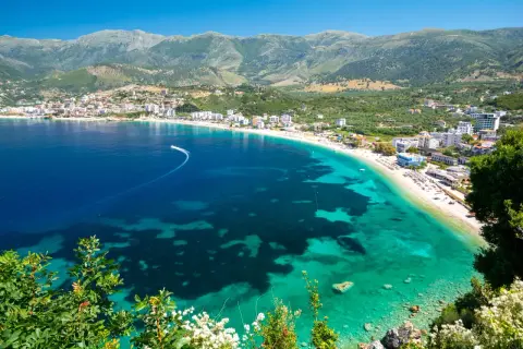 Malownicze wybrzeże riwiera albańska z turkusową wodą, piaszczystą plażą i górami w tle.