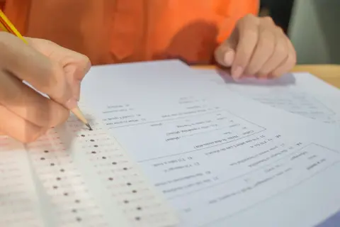 Ręka z ołówkiem zaznacza odpowiedzi na arkuszu testowym. Zastanawiasz się, ile punktów na maturze z matematyki zdobędziesz?