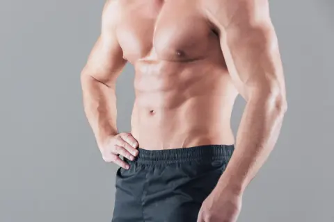 Ein naturaler Bodybuilder mit definierten Bauchmuskeln und Armen steht im Profil.