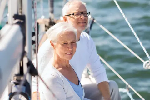 Uśmiechnięta para seniorów na żaglówce. Idealne wczasy świąteczne dla samotnych seniorów, by poczuli się jak na romantycznym rejsie.