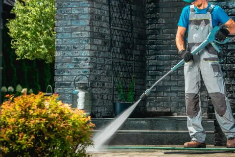 Mężczyzna w ogrodniczkach wykonuje impregnację kostki brukowej myjką ciśnieniową, chroniąc nawierzchnię przed zabrudzeniami i wilgocią.