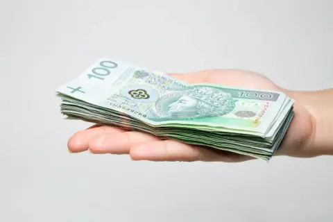 Dłoń trzyma stos banknotów 100 zł. To wstępny zstępny kapitał na nowy projekt.