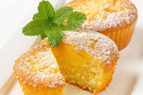Två fluffiga citronmuffins, pudrade med florsocker och garnerade med mynta. Perfekt för ett enkelt citronmuffins recept.