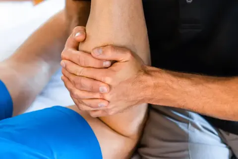 Mains expertes prodiguant un massage après sport sur une jambe. Soulagement musculaire garanti.