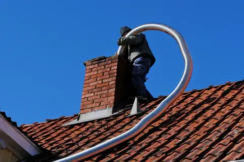 Un couvreur effectue l'installation tubage cheminée sur un toit en tuiles rouges, sous un ciel bleu éclatant.