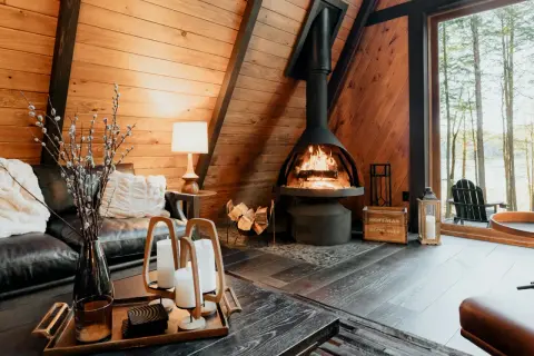 Salon cosy avec cheminée ventouse crépitante, canapé en cuir et vue sur la forêt.