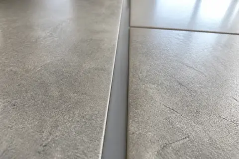 Gros plan sur un joint de dilatation carrelage gris, entre deux carreaux texturés.
