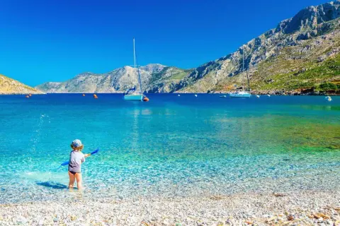 Dziecko bawi się na kamienistej plaży w Grecji. Marzysz o tanich lotach z Krakowa gdziekolwiek? To miejsce czeka!