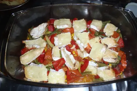 Zapiekanka z warzywami i kawałkami sera camembert w szklanym naczyniu.