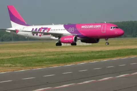 Samolot Wizz Air z różowym kadłubem i fioletowym ogonem na pasie startowym.