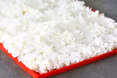 En stor mängd perfekt kokt **sushi ris** sprids ut på en röd bricka, redo att bli till läckra rullar.