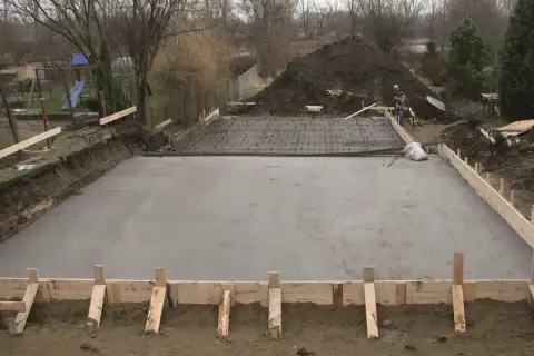 Plac budowy z wylana płytą betonową, przygotowywaną pod fundamenty. Widoczne zbrojenie i szalunki. Klasy ekspozycji betonu są kluczowe dla trwałości.