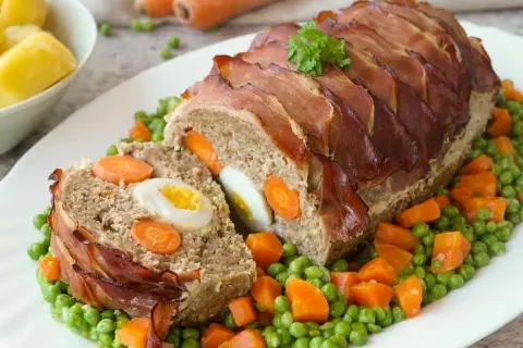 Ein saftiger falscher Hase, umwickelt mit Speck, serviert auf Erbsen und Karotten.