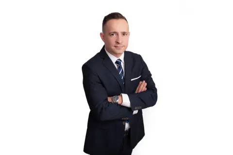 Mężczyzna w garniturze ze skrzyżowanymi rękami, na białym tle.