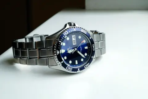 En blå dykarklocka, Orient Ray II, med ett silverfärgat armband ligger på en vit yta.