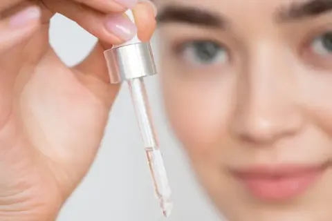 Mujer sosteniendo un gotero con líquido transparente cerca de su rostro.