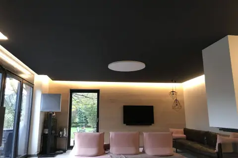 Nowoczesny salon z czarnym sufitem napinanym. Widać subtelne wady w postaci delikatnych zagnieceń na jego powierzchni.