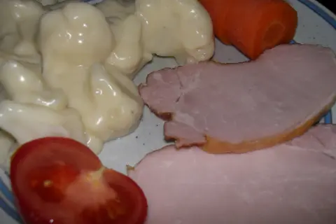 En tallrik med stuvad blomkål, skinka, en morot och en tomatklyfta. En klassisk svensk husmansrätt.
