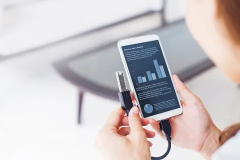 Kobieta podłącza pendrive do smartfona, pokazując, jak włączyć funkcję OTG. Na ekranie telefonu widoczny wykres i tekst.