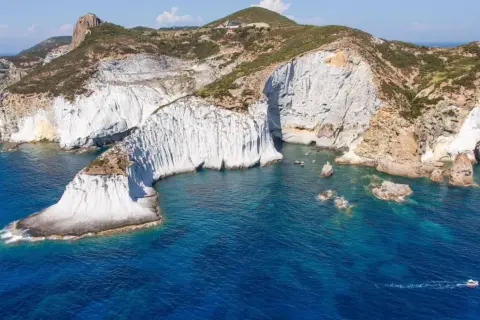 Scogliere bianche a picco sul mare blu intenso di Ponza. Un piccolo gozzo solca le acque cristalline, mentre la natura scolpisce la costa.