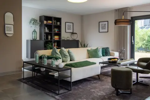 Modernes Wohnzimmer mit beigem Sofa, grünen Akzenten und hellgrauen Wänden. Diese Wandfarben sind modern und schaffen eine ruhige Atmosphäre.