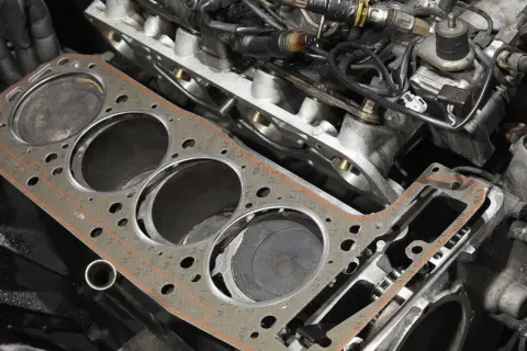 Nowa uszczelka pod głowicą czeka na montaż. Widać cylindry silnika i fragmenty osprzętu.