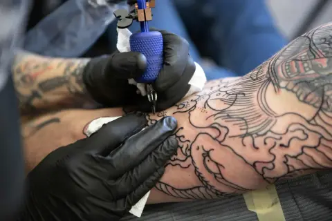 Artysta w czarnych rękawiczkach tworzy na ramieniu skomplikowany wzór irezumi, dodając kolejne linie do smoka i fal.
