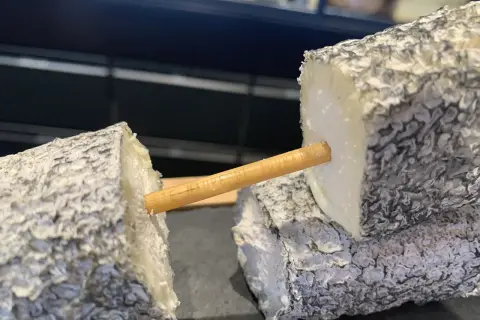Deux morceaux de fromage de chèvre, un "tête de maure", sont reliés par un bâtonnet en bois.