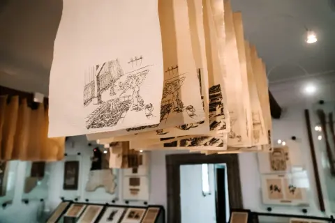 Rzędy ręcznie rysowanych scen na papierze czerpanym wiszą pod sufitem, tworząc unikalną galerię.