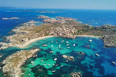 Vue aérienne d'une **excursion île Lavezzi** : eaux turquoise, plages de sable fin, rochers granitiques et nombreux bateaux au mouillage.