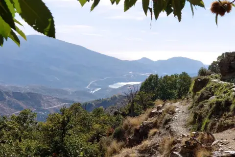Sendero rocoso con vistas a montañas y un embalse, ideal para rutas senderismo Alpujarra.