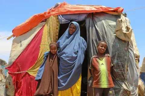 En kvinna och två barn står framför ett provisoriskt boende i Somalia. Deras historia är en del av Somalias historia.