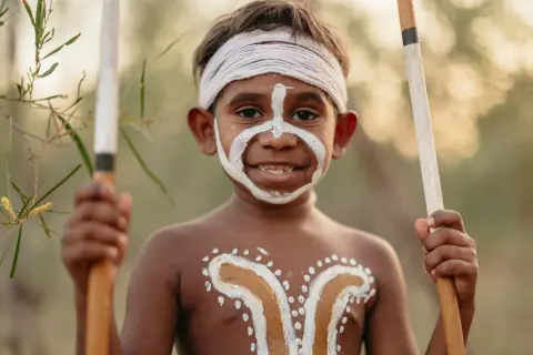 Giovane membro del popolo australiano con pittura facciale e corporea tradizionale, impugna lance.