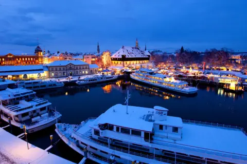 Schneebedeckte Schiffe im Hafen von Konstanz, beleuchtet vom Glanz des Weihnachtsmarktes.