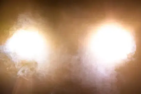 Deux halos lumineux, couleur feu de croisement, traversent une brume légère.