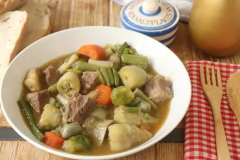 Un reconfortante plato de menestra de ternera con trozos de carne tierna y verduras como alcachofas, judías verdes y zanahorias.
