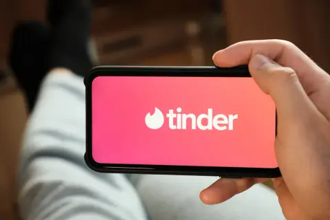 Dłoń trzyma smartfon z otwartą aplikacją Tinder.