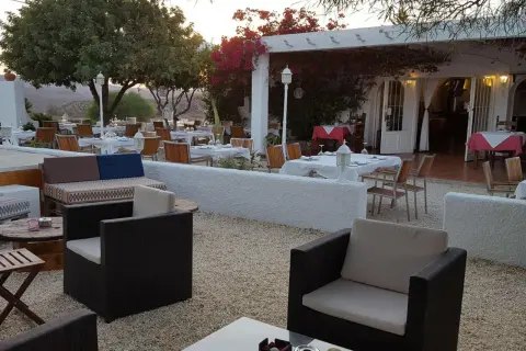 Mesas puestas en el exterior de un restaurante con un bar aguamarga. Ambiente tranquilo bajo la luz del atardecer.