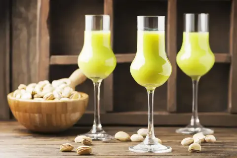 Zielony likier pistacjowy w kieliszkach, obok miseczki z pistacjami. Idealny przepis, jak zrobić wódkę ze spirytusu, by uzyskać taki smak.