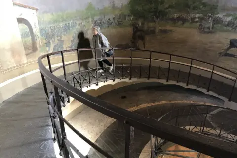 Una persona sale la scala a chiocciola all'interno della torre di San Martino, con un affresco di battaglia che decora le pareti.