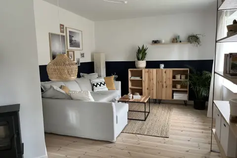 Salon moderne avec canapé gris, meuble en bois et tapis en jute. Le mur est peint en deux tons, blanc et bleu nuit, rappelant des techniques de peinture acrylique.