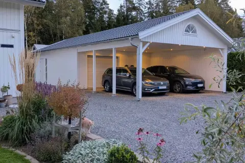 Vitt garage med två bilar under taket. En katt smyger i rabatten framför. Perfekt för att bygga garageport.