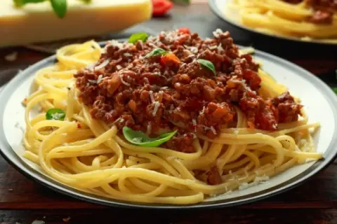 Pyszne spaghetti bolognese, idealne danie, gdy zastanawiasz się, co zrobić z makaronu spaghetti. Posypane parmezanem i listkami bazylii.